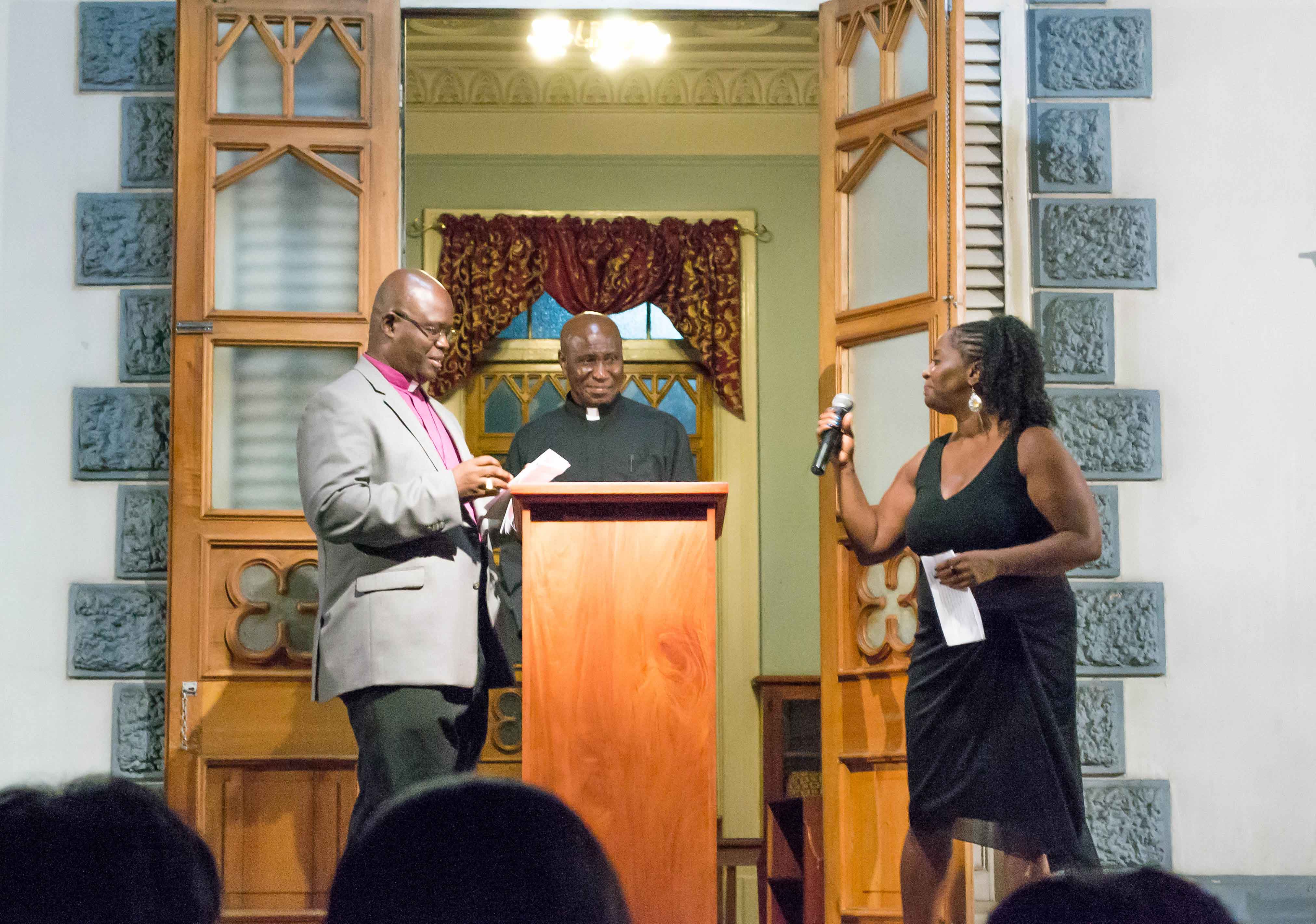 Master of Ceremonies, Magella Moreau, shares a light moment with Trinidad and Tobago’s Anglican Bishop, the Rt. Reverend Claude Berkley, and chairman of the Hayes Court Restoration Committee, Father Eric Thompson, during the evenings proceedings.